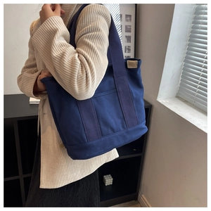 Detail of dark blue canvas tote bag featuring front dual pockets and woven top handles