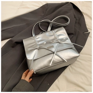 Detail of silver metallic textured handbag with bow accents on grey blazer background