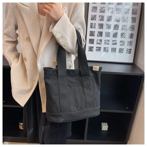 Close-up of black canvas tote bag featuring large front pocket and reinforced stitching