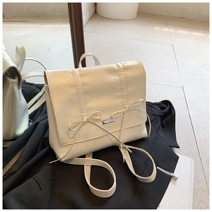 Detail of cream pleated backpack with bow accents on a stylish black blazer background