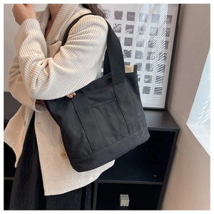 Detail of a large black canvas tote bag with wide shoulder straps shown on a model