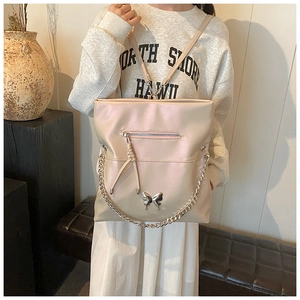 Detail of light beige tote bag with silver butterfly charm and chain strap decoration