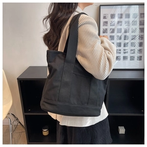 Model wearing a large capacity black canvas tote bag for daily commute and casual style