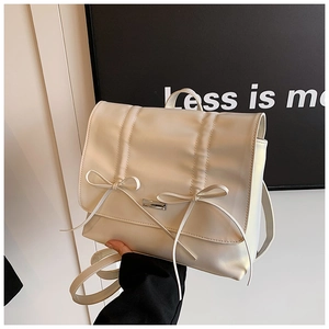 Detailed close-up of cream pleated backpack with decorative bows and silver buckle