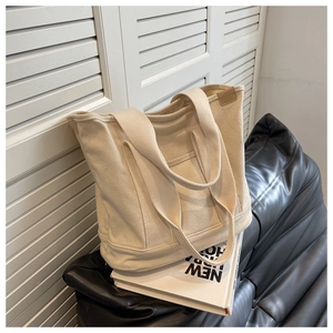 Close-up of minimalist cream canvas tote bag with brown leather label and double straps