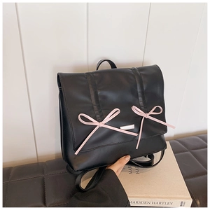 Close-up of black pleated backpack with pink ribbon bows and silver logo plaque