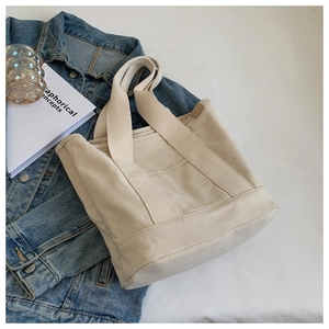 Detail of minimalist beige canvas tote bag with reinforced straps on denim jacket