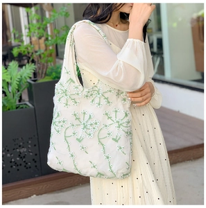 Detail of white mesh tote bag with green floral embroidery and lightweight handle