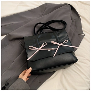 Detail view of black matte leather bag with soft pink bows and silver logo plaque