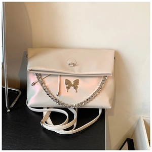 Close-up of cream-white tote bag featuring silver butterfly charm and chunky metal chains