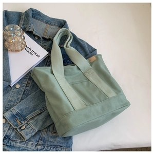 Detail view of a light green canvas tote bag with thick texture and faux leather tag