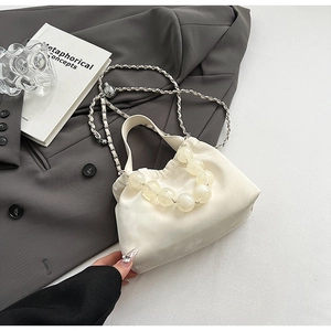 Minimalist cream cloud handbag with pearl bead handle and woven chain strap on grey blazer