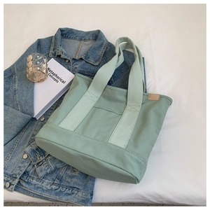Detail of mint green canvas tote bag on white fabric with book and denim jacket accessory