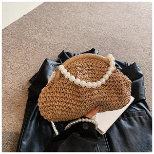 Détail d'un sac en paille tissée avec deux poignées en perles blanches sur cuir noir