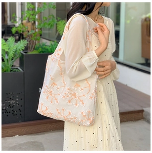 Detailed close-up of white mesh tote bag with orange floral embroidery in outdoor sunlight