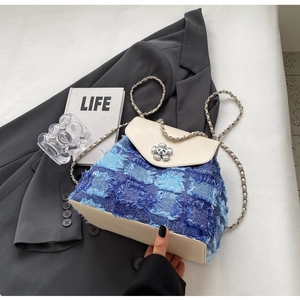 Detailansicht der Denim-Patchwork-Beuteltasche mit Blumen-Metallverschluss auf grauem Sakko