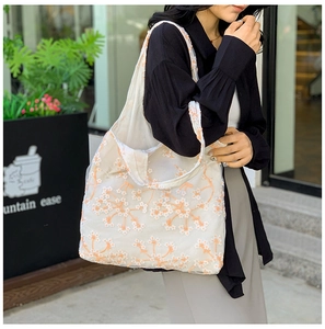 Detail of floral embroidery on a white mesh tote bag held by a model in a café setting