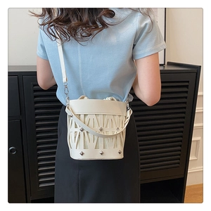 Detail of white hollowed-out bucket bag with metal studs and drawstring inner pouch