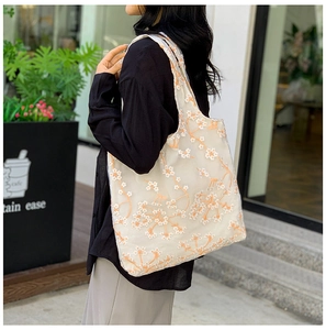Detail of white mesh tote bag with delicate orange floral embroidery and semi-transparent texture