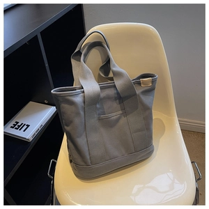 Detail of grey canvas tote bag showing thick fabric texture and front pocket on white chair