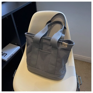 Detail of dark grey canvas tote bag with reinforced handles and front pocket on chair