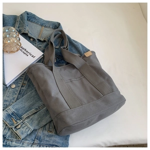 Detailed view of grey canvas tote bag with leather trim and wide straps on denim background