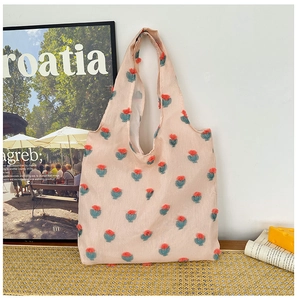 Close-up of pink tote bag with orange floral embroidery and green stems detail