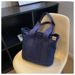 Detail of navy blue canvas tote bag showing front pocket and durable wide shoulder strap