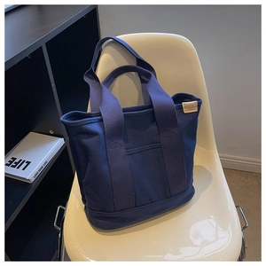 Detail of dark blue canvas tote bag with front pocket on a white minimalist chair