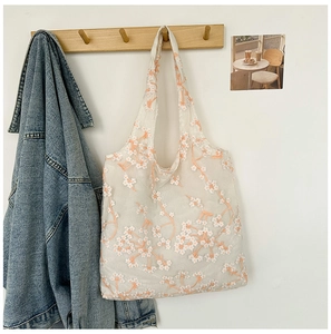Detailed close-up of white mesh tote bag with delicate floral embroidery on wooden hook