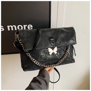 Detail of black cracked leather tote bag featuring a silver chain and butterfly hardware
