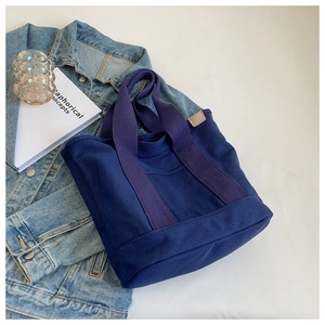 Flat lay of large navy canvas tote bag with leather tag detail and lifestyle accessories