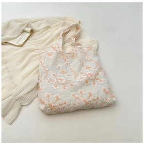 Close-up of mesh tote bag featuring orange daisy embroidery and translucent fabric texture