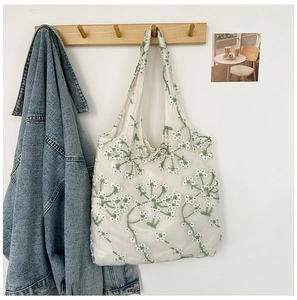 Detail of white mesh tote bag with green floral embroidery hanging on a wooden hook