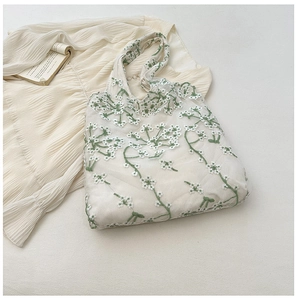 Detail of floral lace embroidery on cream mesh tote bag with green leaf patterns