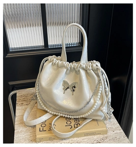 Detalle del bolso de hombro blanco con mariposa, cadena de perlas y textura plisada