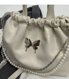 Detalle de bolso plisado crema con mariposa plateada y correa de perlas y cadena