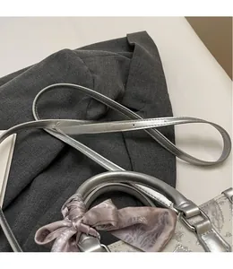 Detail einer silbernen Prägehandtasche mit verstellbarem Gurt und lila gemustertem Seidentuch