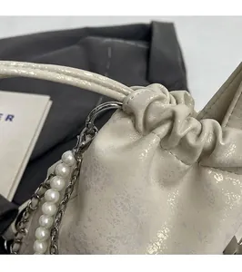 Detalle del bolso plisado nacarado con elegantes cadenas de perlas y metal plateado