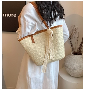 Detailed back view of a woven straw tote bag with brown leather straps and lace bow