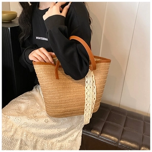 Detail of woven straw tote bag with brown leather handles and white lace decorative ribbon