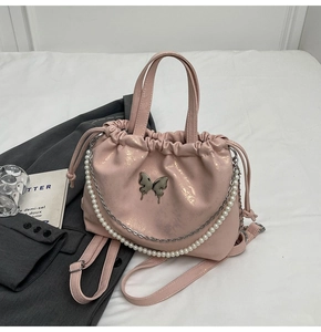 Detalle de bolso saco rosa con cordón con dije de mariposa plateada y cadena perlas