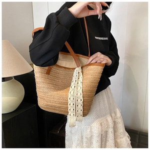 Detail of woven straw tote bag with brown leather handles and decorative white lace ribbon