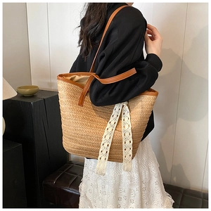 Detail of a large woven straw tote bag with lace ribbon and leather straps shown on model