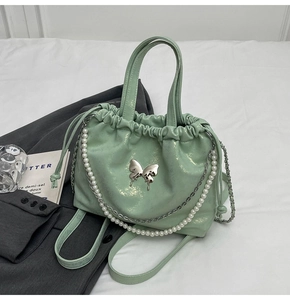 Detalle de bolso verde menta con adorno de mariposa y cadena de perlas finas