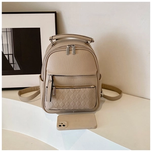 Detail of beige mini backpack with litchi texture and quilted front pocket next to phone