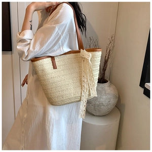 Detail of beige straw tote bag with brown leather handles and a white lace bow detail