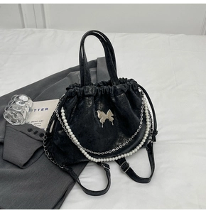 Detalle de mochila negra mate con mariposa plateada y cadena de perlas decorativa