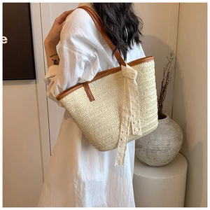 Detail view of woven straw tote bag with brown leather straps and white lace ribbon deco