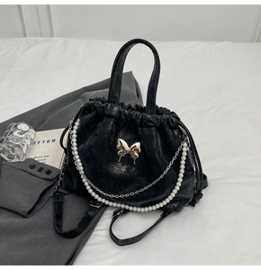 Detalle de bolso negro de cordón con mariposa plateada y cadena de perlas elegante